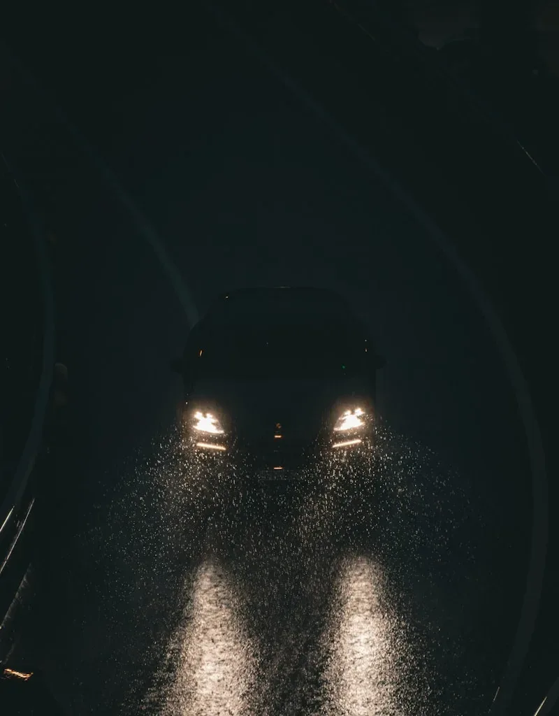 Car headlights illuminate a wet road at night